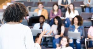 A nurse educator speaking to a diverse group of students in a university lecture hall, highlighting Oregon’s investment in nursing faculty development.
